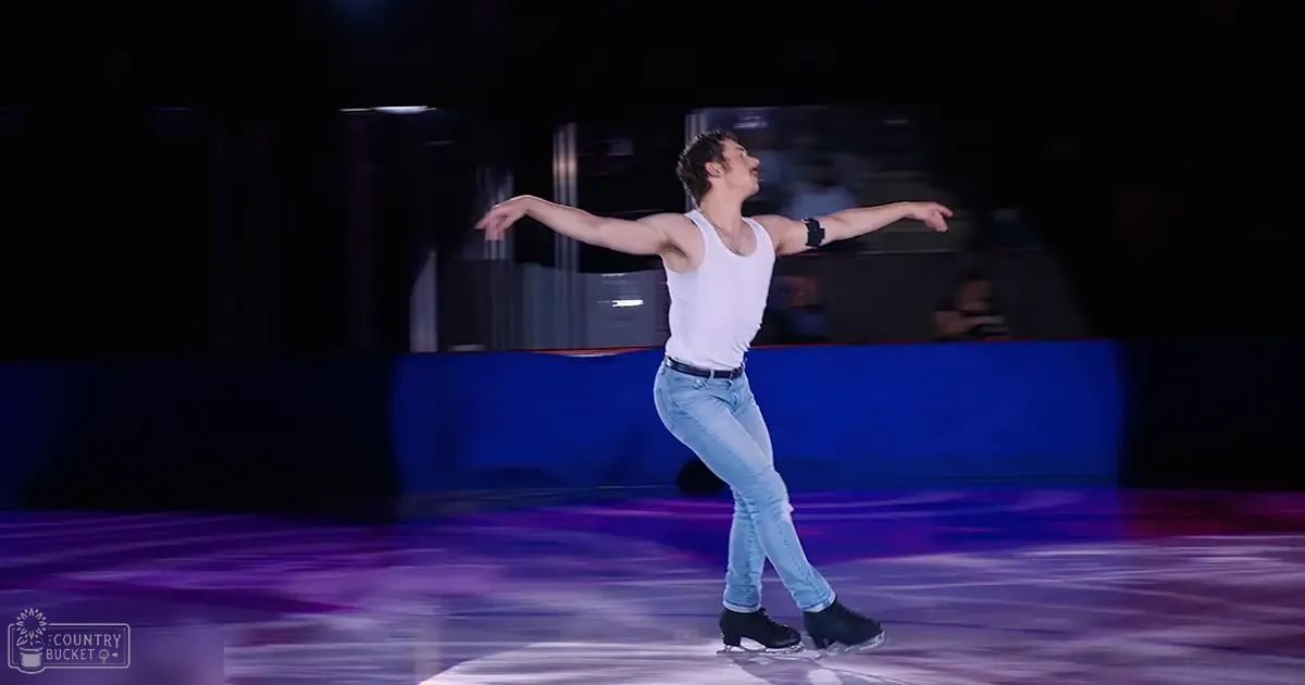 A young adult male figure skater in a white tank top performing at an indoor ice rink under artificial lighting.