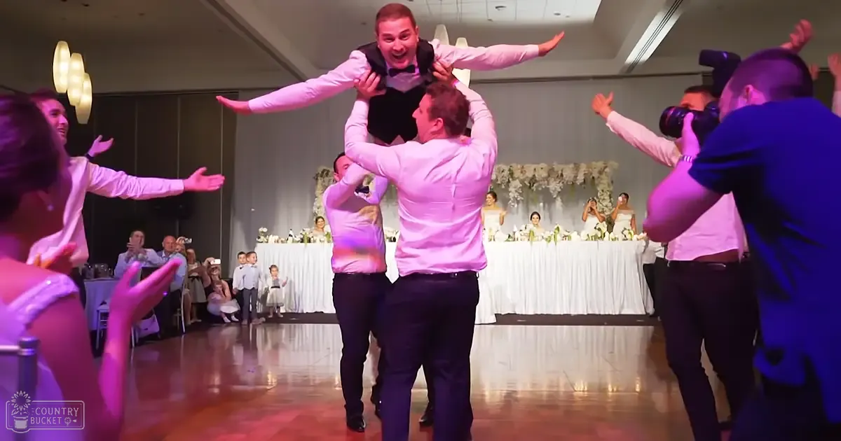 Wedding reception with a group of men performing a lift, seated guests in formal attire, indoor evening setting