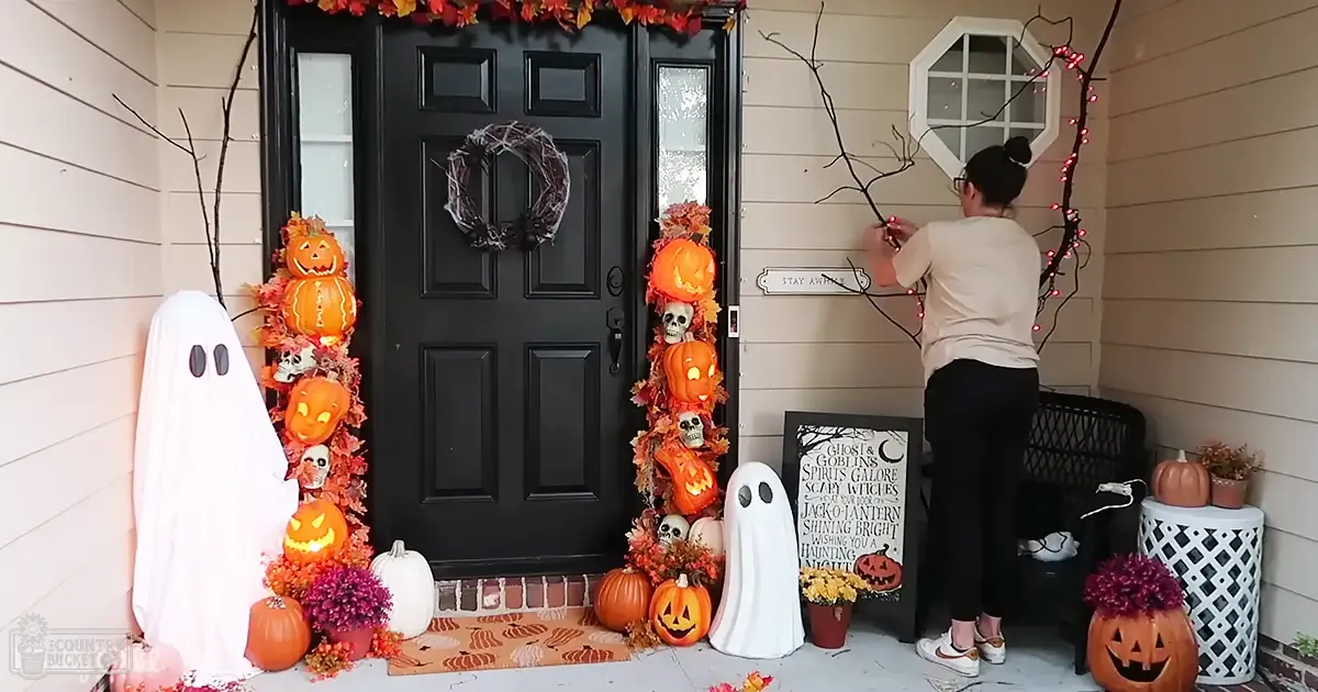 A residential porch decorated for Halloween with string lights, pumpkins, and autumn leaves during daytime.