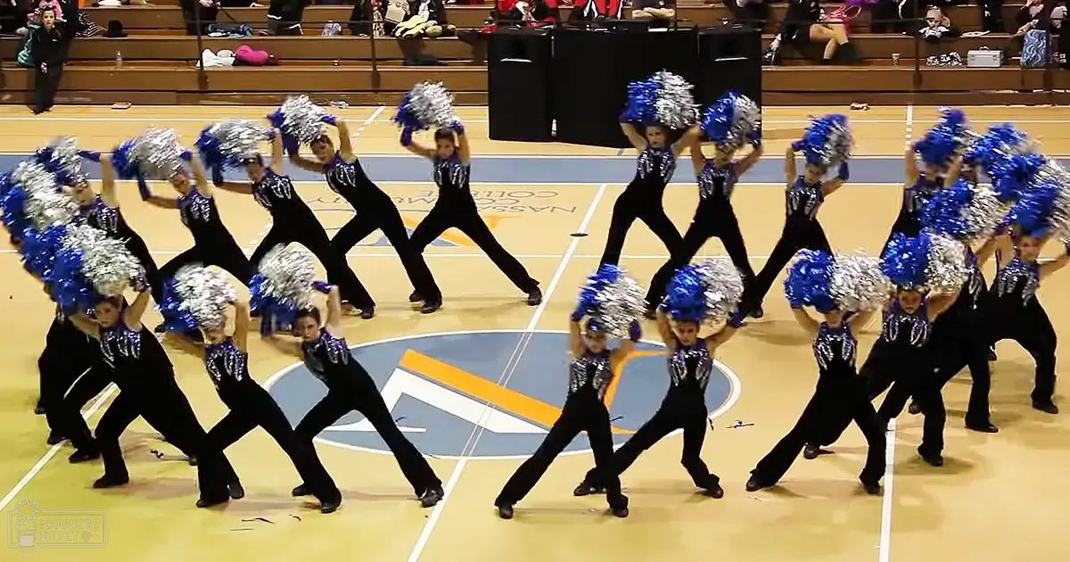 A cheerleading team performs at Nassau Community College during a competition or performance with spectators seated on bleachers and equipment like speakers visible.