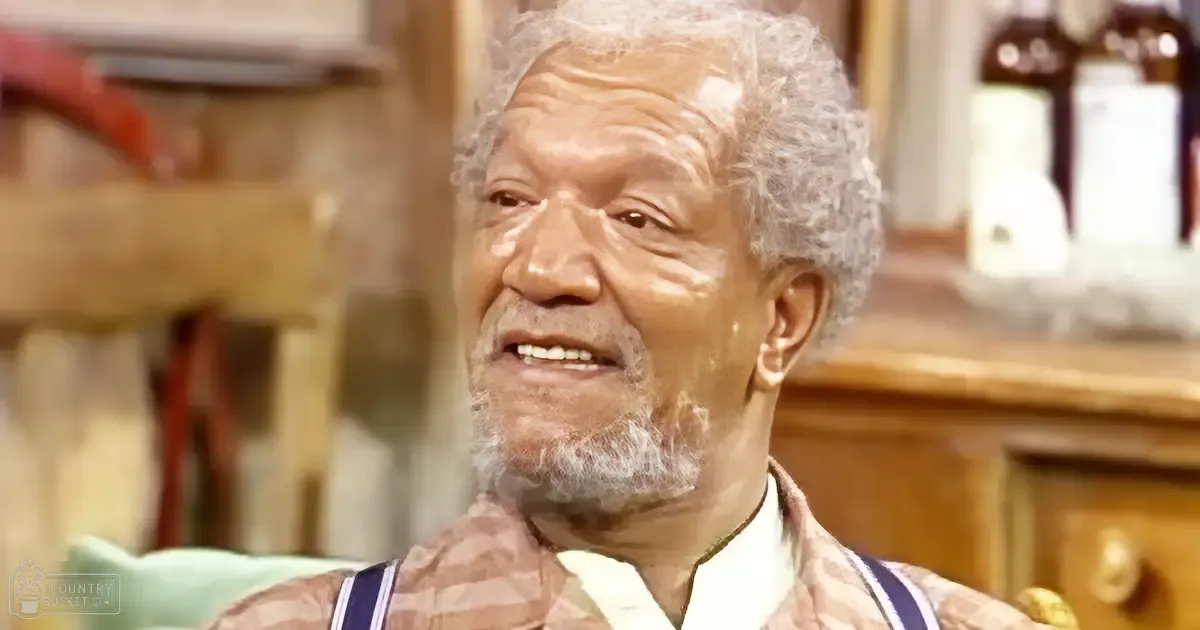 An older adult male in a domestic kitchen setting with striped suspenders and a white-collared garment.