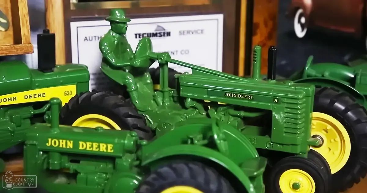 Two John Deere 630 model toy tractors with a farmer figure seated on one, displayed indoors in a store or exhibition space for farm equipment.