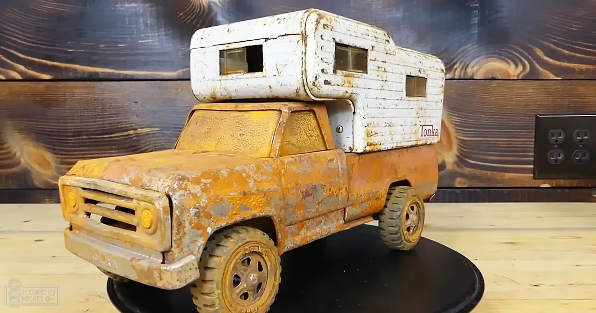 A toy truck with an attached camper with 'Tonka' branding, set against a rustic wooden wall background indoors.