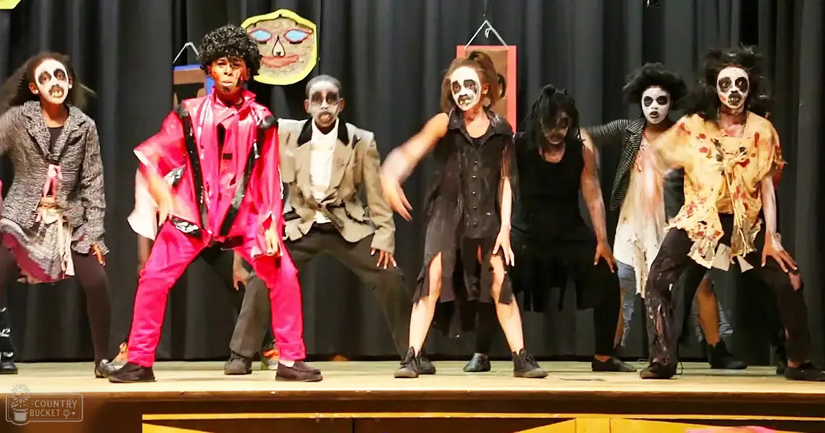 Theatrical performance in a school auditorium with children and adults dressed as zombies or undead characters under dim lighting.