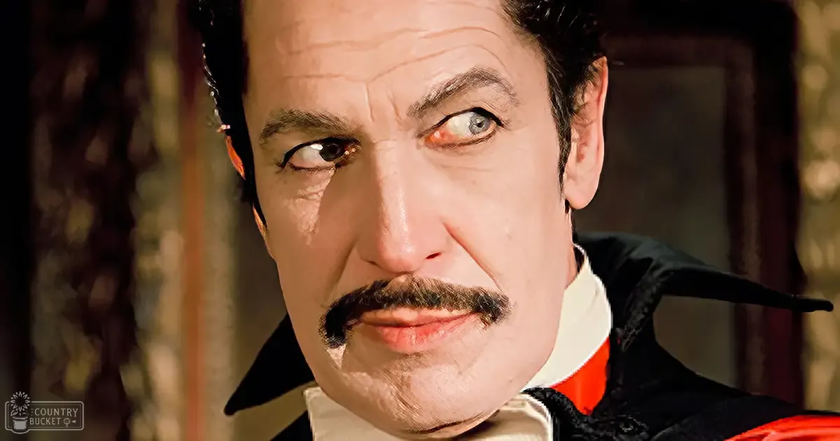 A middle-aged man in 18th-century attire, wearing a black and red coat with white shirt collar, indoors under natural light.