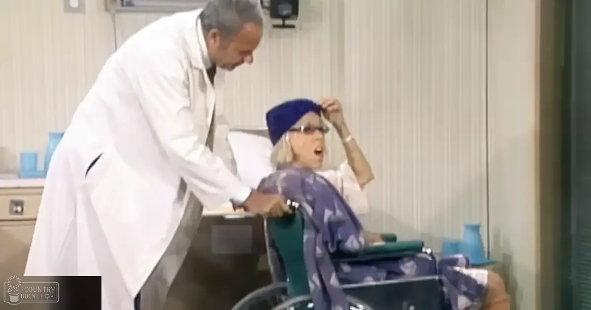 An older female patient with a dark blue headscarf and glasses interacts with a middle-aged male doctor in a medical setting.