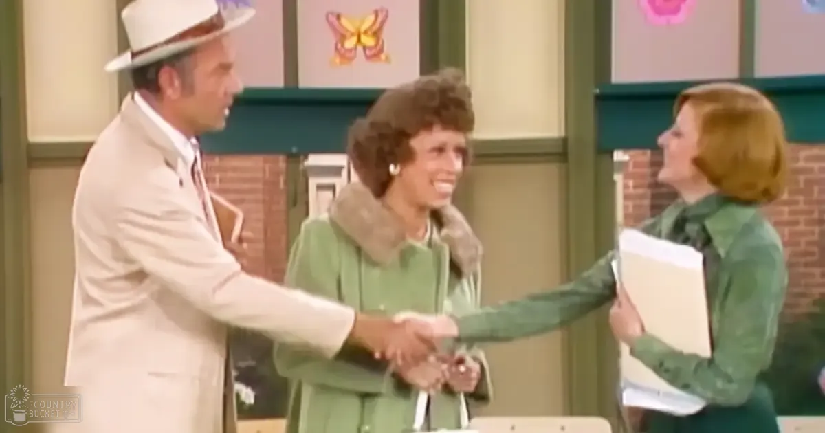 Television show scene set indoors with adults in formal attire, framed artwork with butterflies, green coats, beige suit jackets, white hats, and even lighting.