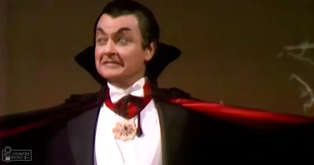 An adult male in a theatrical tuxedo with a red cape performs on stage.