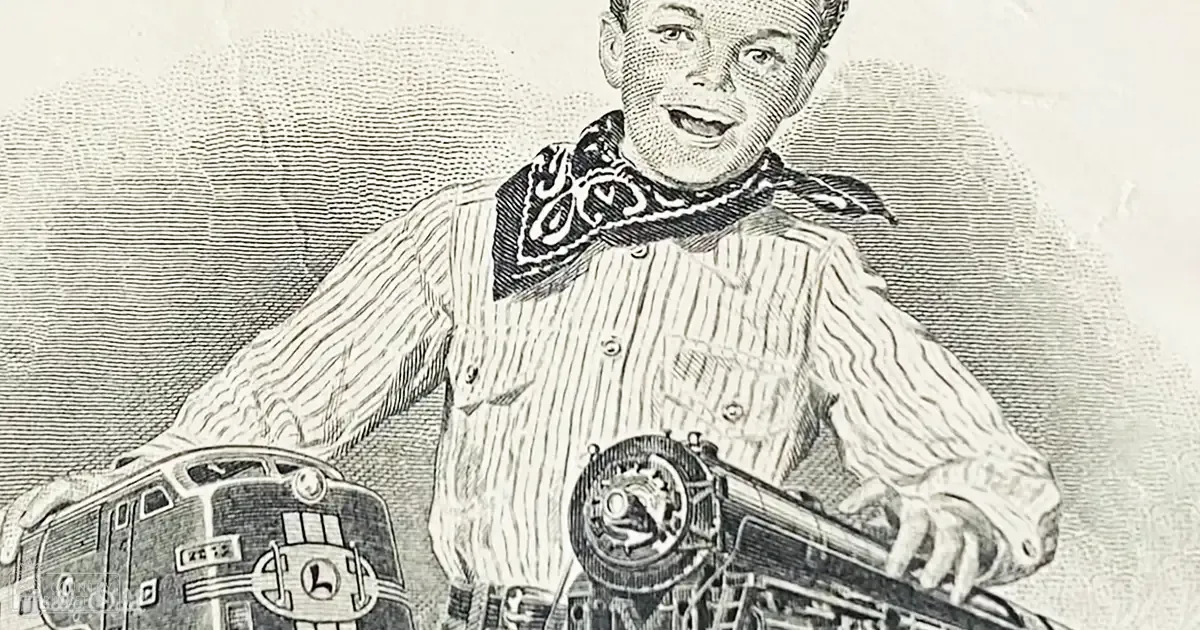 A young adult male in an indoor setting wears a striped shirt with a bandana around the neck, holding what appears to be a mechanical device near a train engine.