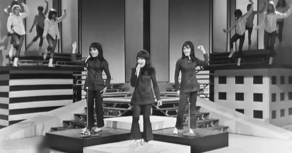A mid-20th century television studio set for a musical performance with stylized architectural elements in the backdrop, bright indoor lighting.