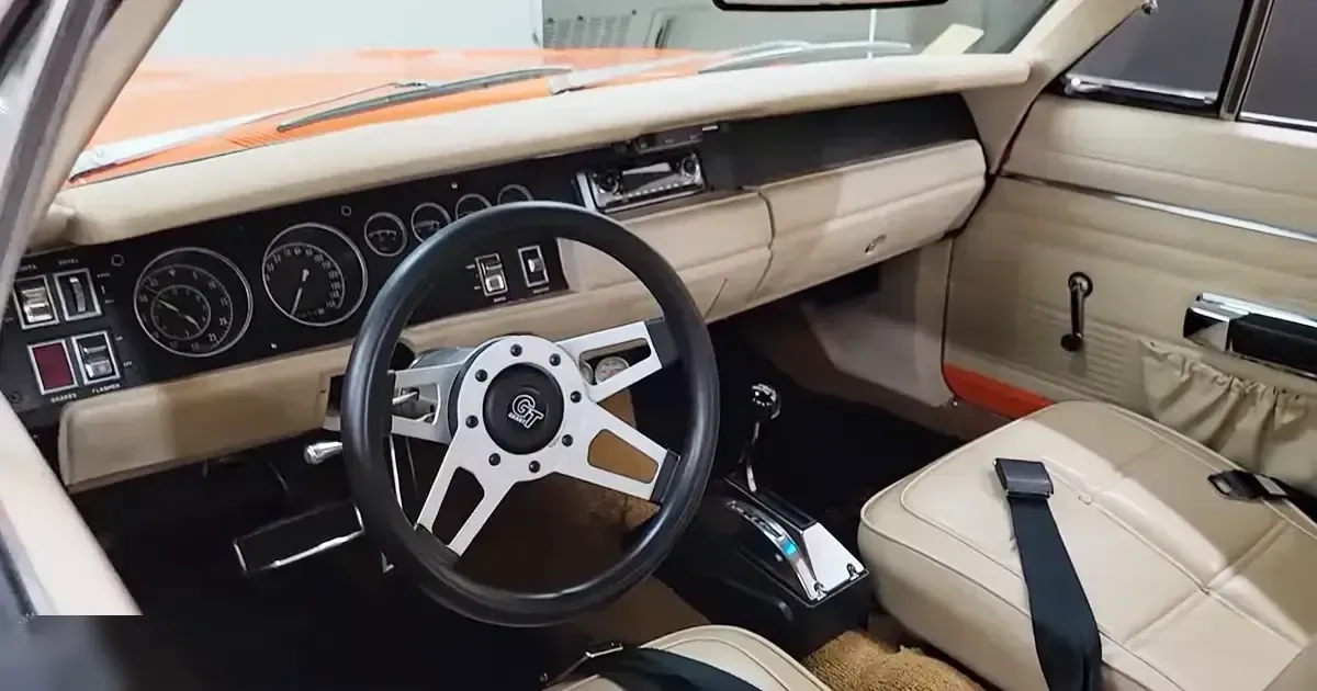 A vintage car interior with beige seats and dashboard, orange accents on the roof, and a clean indoor setting.