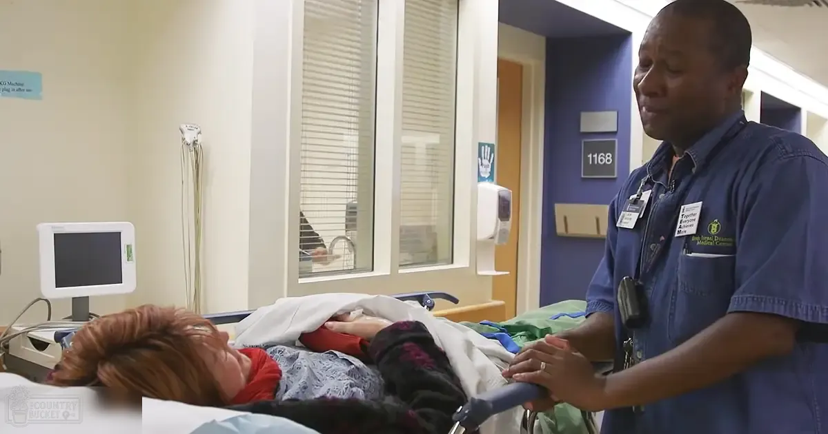 Healthcare worker interacting with older adult female patient in a hospital room, natural light streaming through blinds.