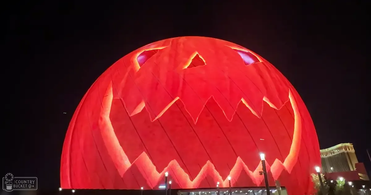 A large illuminated red pumpkin structure with triangular cutouts resembling teeth and eyes, set against part of the Las Vegas skyline at night.