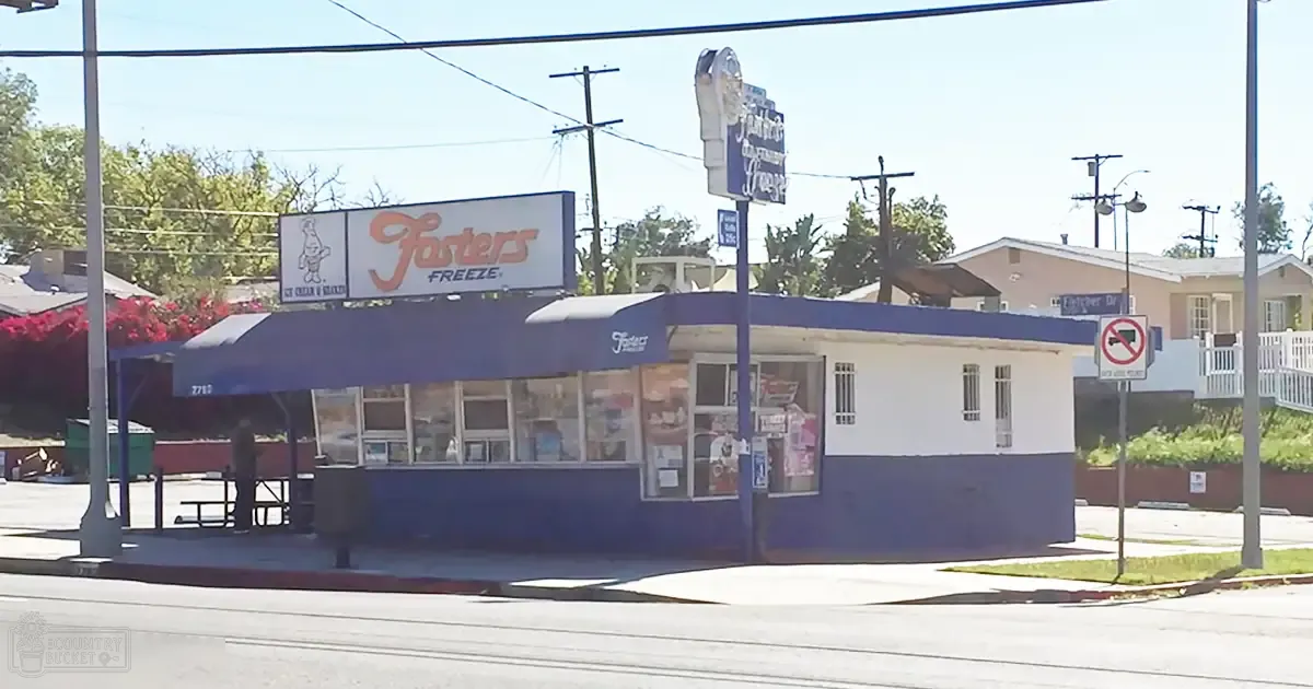 Foster's Freeze ice cream shop in an urban area with residential homes, a picnic table under a canopy, and clear daylight lighting.