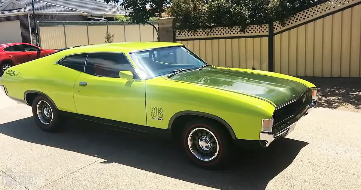 A classic Ford Torino muscle car parked in a residential driveway, surrounded by greenery under clear daylight conditions.