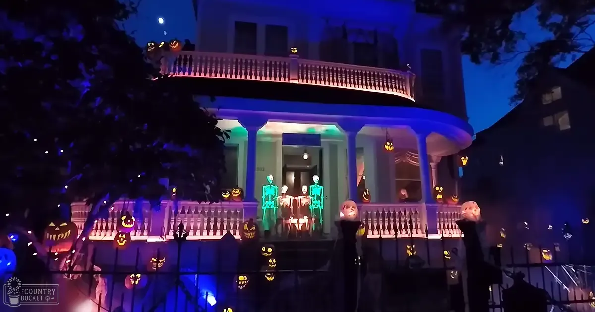 Halloween decorations adorn a classic urban residential home with jack-o'-lanterns, illuminated skeletons, and festive lighting at dusk.