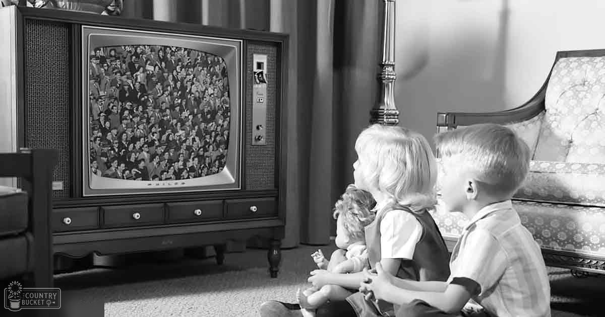 Children watching television in a vintage living room with furniture and a patterned armchair, daytime light.