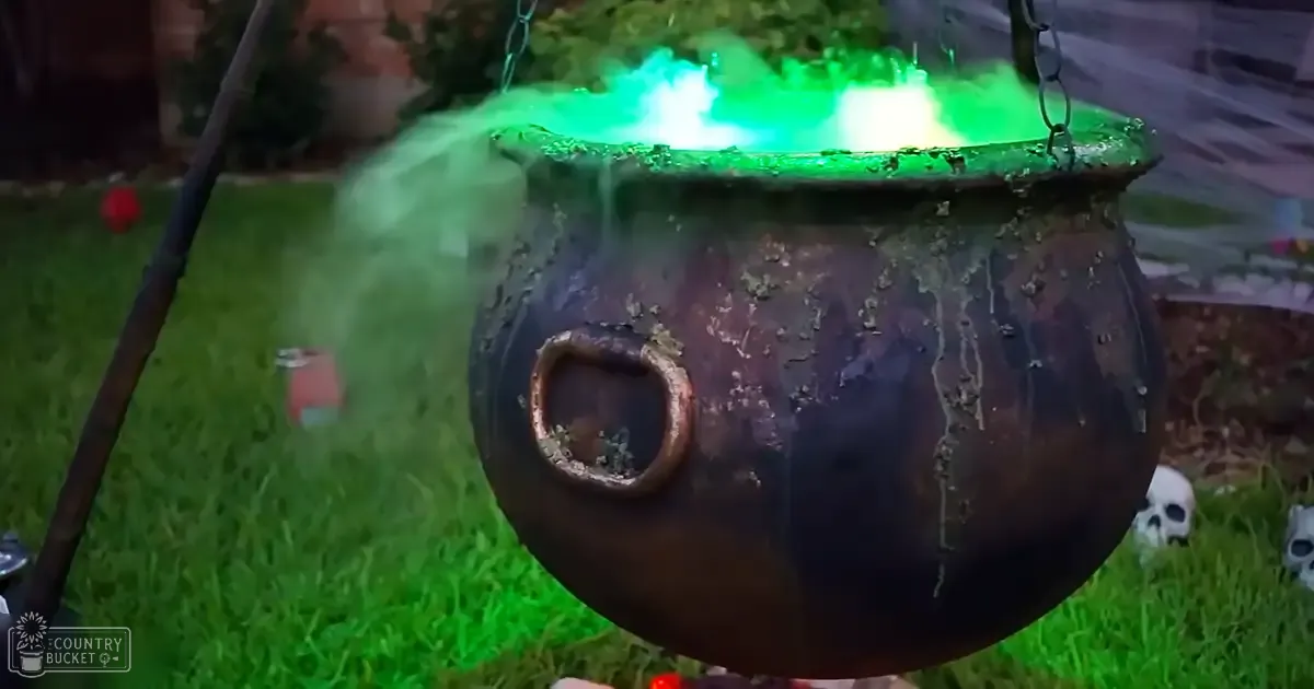 A garden scene with a large dark cauldron emitting green smoke and Halloween-themed decorations in autumn light.