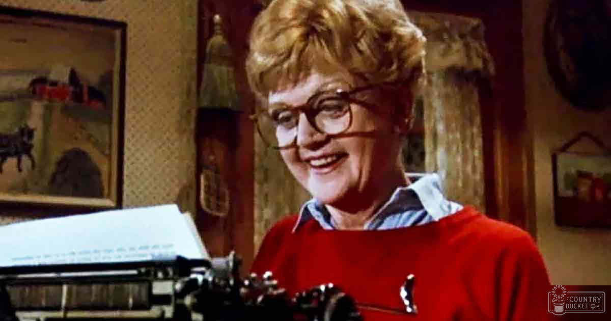 Older adult woman in home setting, red sweater with white collar and blue patterned shirt, mid-20th century decor, typewriter foreground