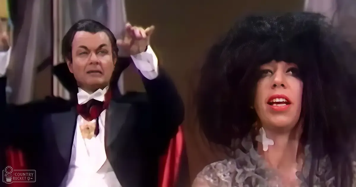 A theatrical performance scene with two characters, a male in a formal black tuxedo with a white shirt and red bow tie, likely from the late 19th to early 20th century, and a female in a lace-trimmed dress with a high neckline and long sleeves, suggesting a vintage style. The setting is an indoor theater or opera house with curtains and stage setup visible.