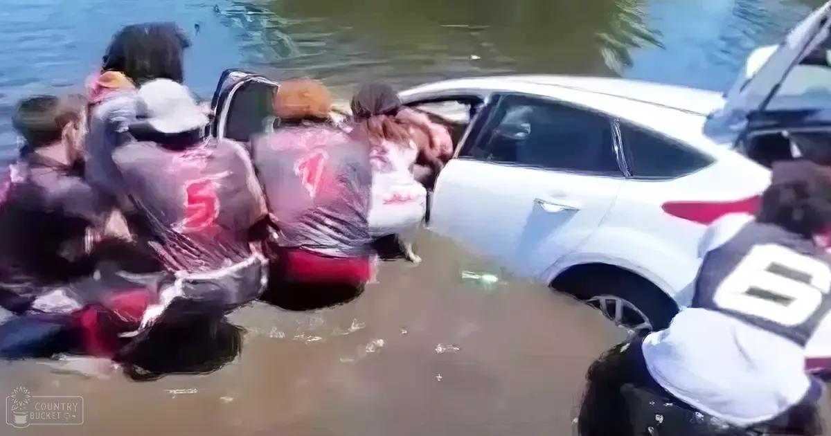 A group of individuals attempting to rescue someone from floodwaters surrounding a white car in an urban area affected by flooding.
