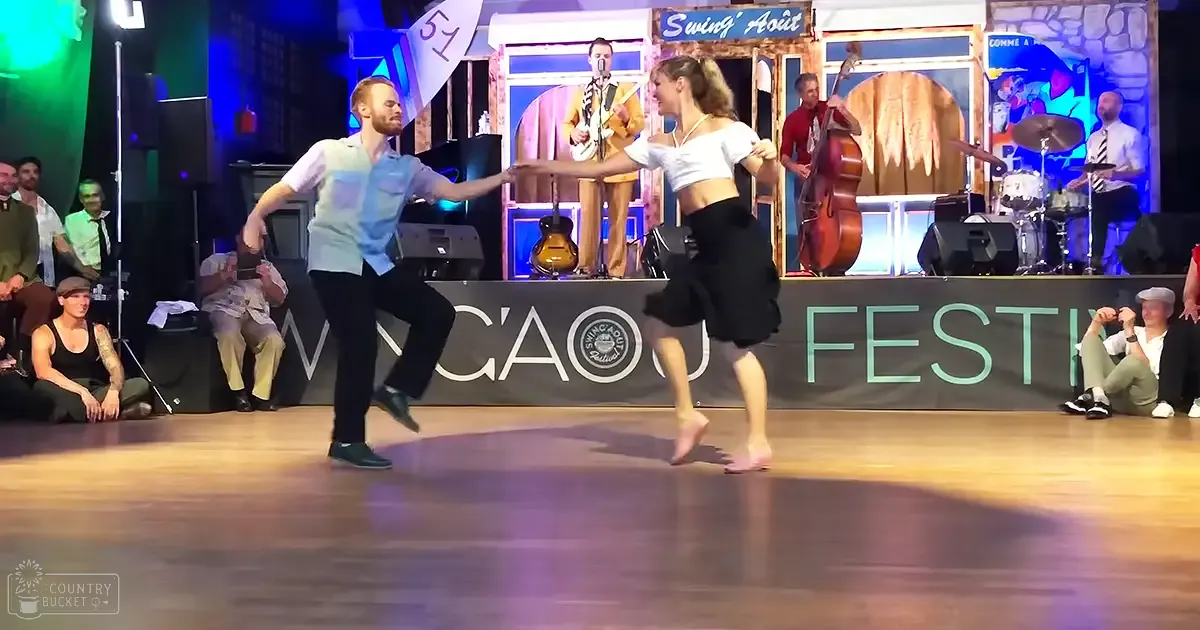 A young couple dances at the 'Swing' Août Festival', an indoor evening event with musical instruments and a 'Swing' Août sign visible on stage.