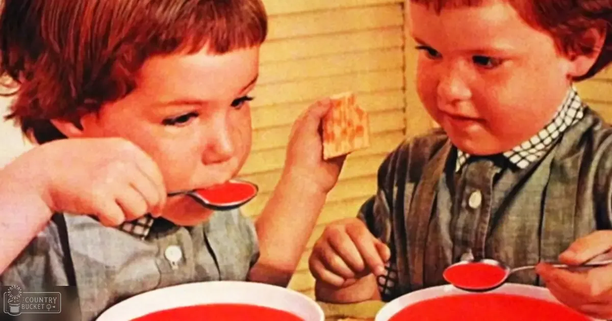 Two children eating soup at a home dining area, wearing plaid button-down shirts with long sleeves and grayish-blue colors; wooden paneling in the background suggests an indoor setting.