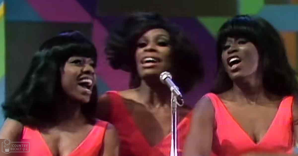 A musical performance scene from the 1960s or early 1970s with young adult females dressed in orange and red sleeveless tops, set against a colorful geometric backdrop.