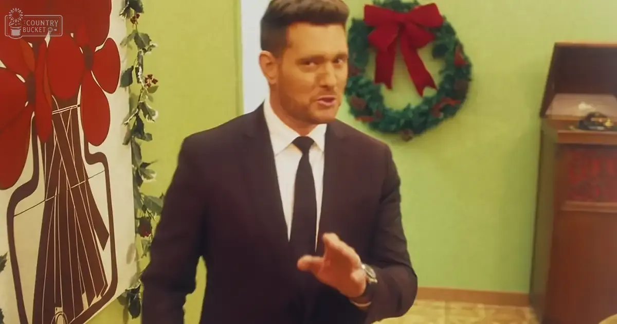 A young adult male in a dark suit jacket, white dress shirt, and black tie stands indoors decorated for Christmas.