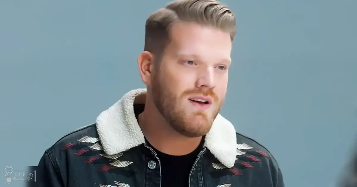 A young adult male in a relaxed fit denim jacket with a high neckline and geometric patterns stands against a plain light blue background.