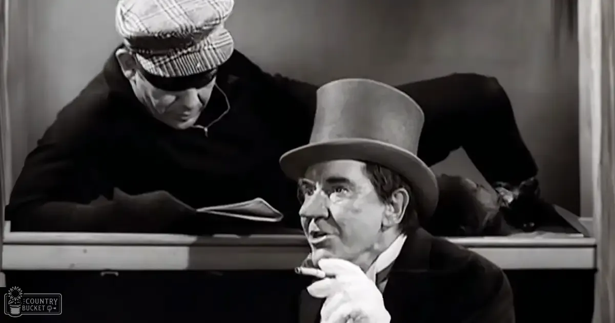 Adult male wearing a dark coat and tall top hat indoors with another individual leaning over him; black cat resting nearby.