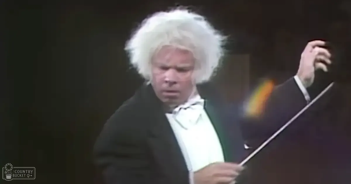 A middle-aged male conductor in a 19th-century tuxedo holding a baton on stage with dark curtains, text reading 'Madly Odd' visible.
