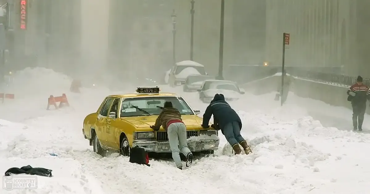 A yellow taxi stuck in deep snow amidst tall urban buildings during a snowy winter day.