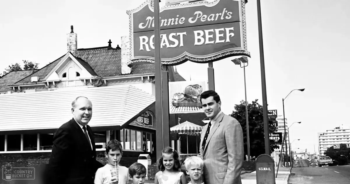A family of four in front of Minnie Pearl's Roast Beef restaurant on a sunny day; adult male wearing dark suit from the 1950s-1960s, child holding drink in clear plastic cup with straw.