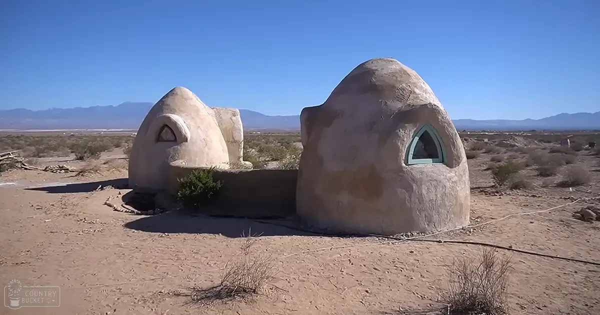 Dome-shaped adobe structures in a barren desert landscape with sparse vegetation under clear blue skies.