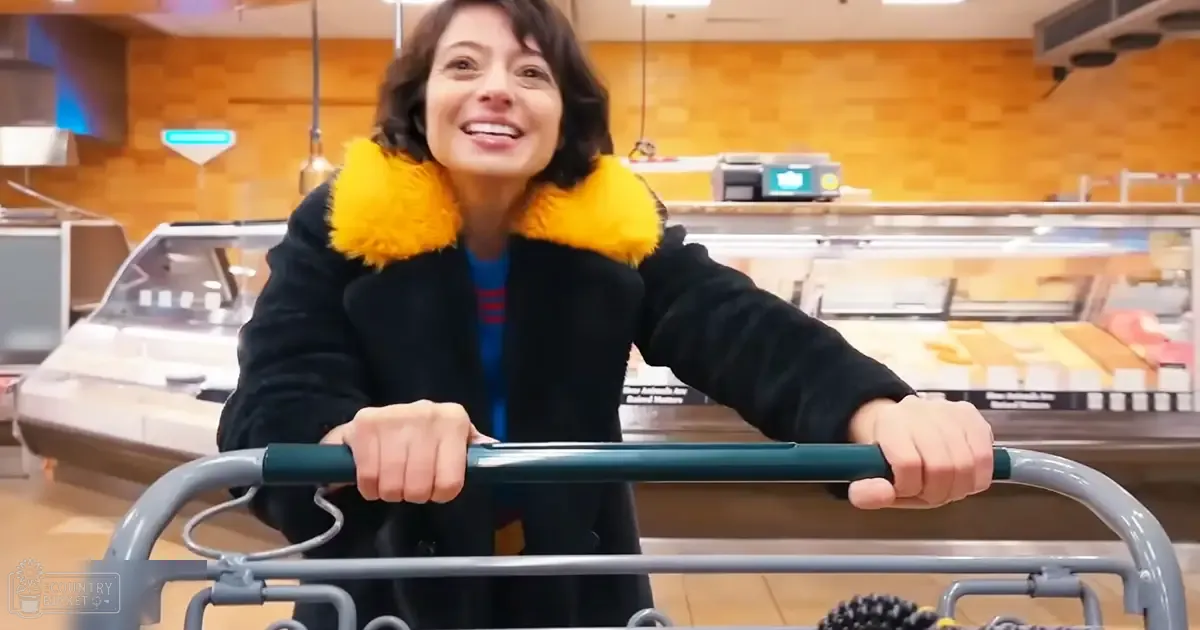 Adult female in a grocery store wearing a black coat with yellow fur trim, shopping for baked goods.