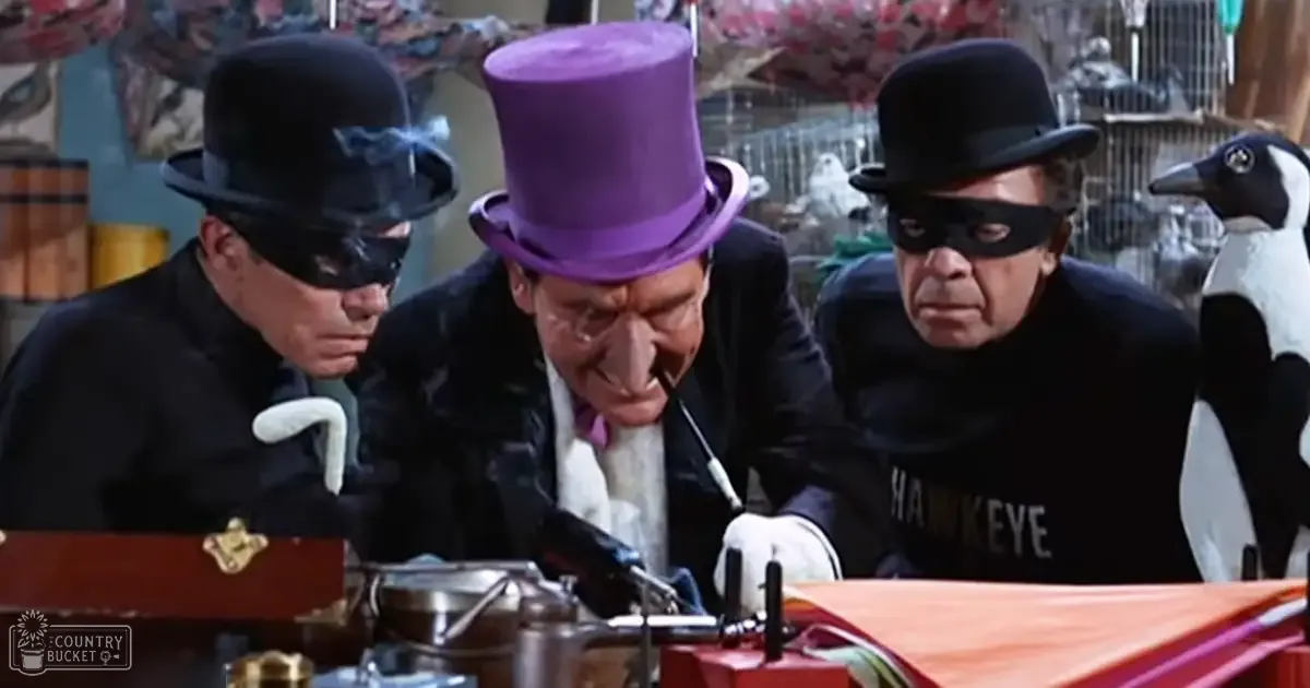 A whimsical indoor setting with adults dressed in theatrical attire, including masks and top hats, alongside decorative elements like a birdcage and a painted backdrop of an outdoor scene.