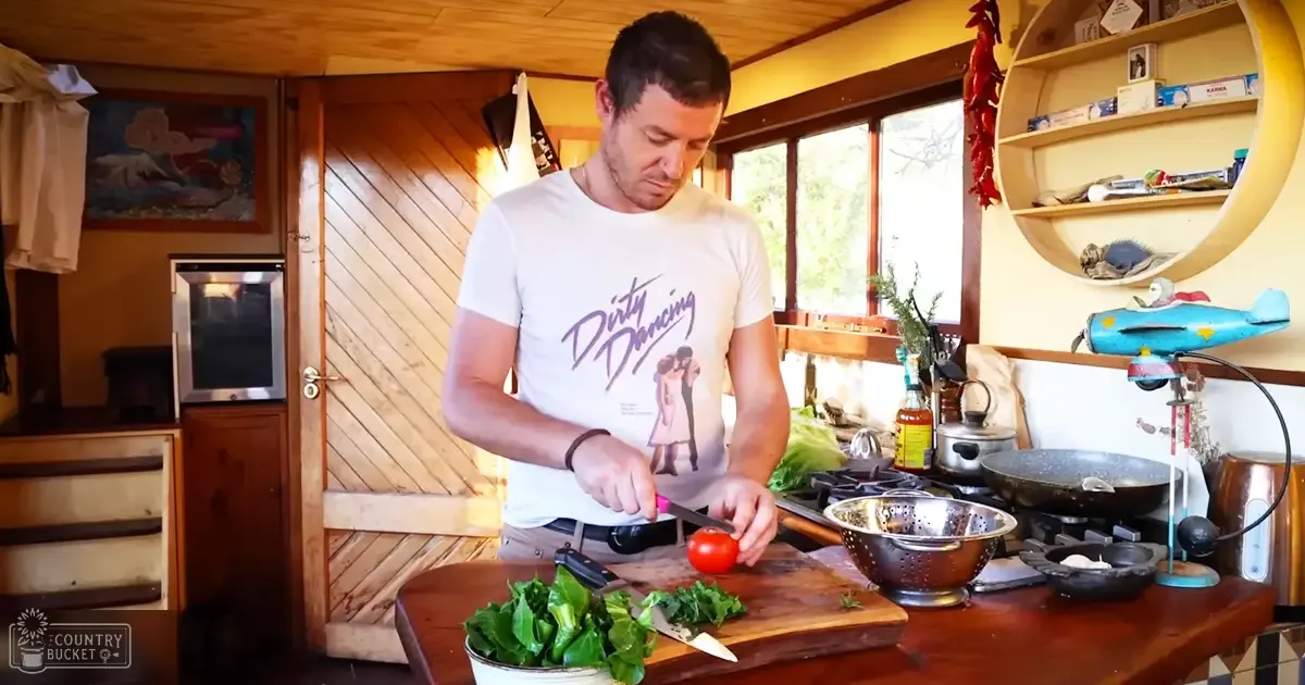 A middle-aged adult male wearing a relaxed fit, crew-neck, short-sleeved t-shirt with a 'Dirty Dancing' graphic print, in a cozy kitchen setting with wooden walls and shelves.