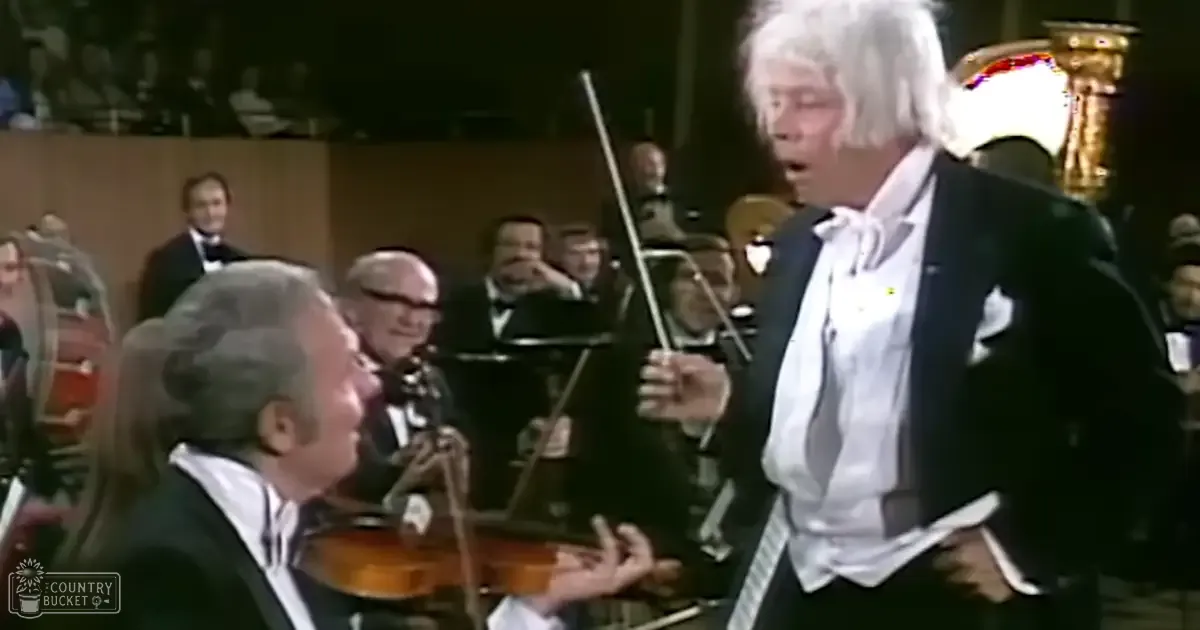 A conductor leading an orchestra during a formal concert performance, with musicians in dark suits and stage lighting highlighting performers.