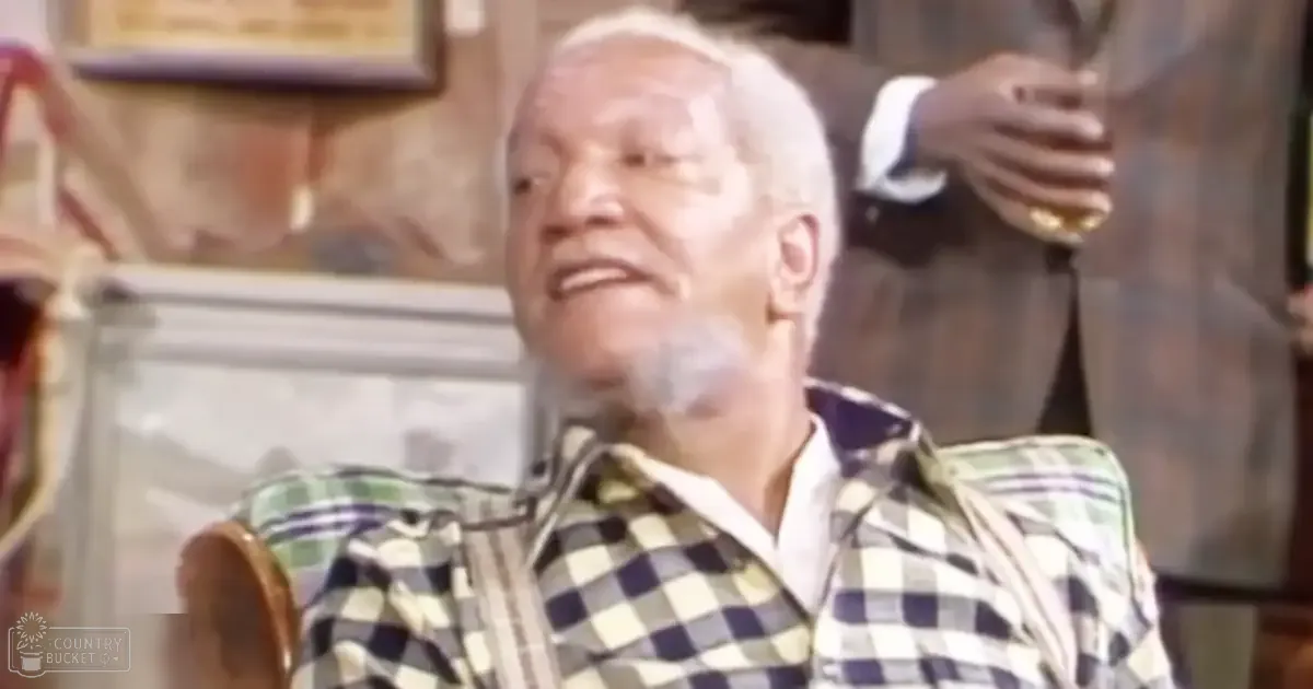 An older adult male sits on a wooden chair inside what appears to be a bar at night with warm lighting, wearing a checkered shirt of dark and light squares.