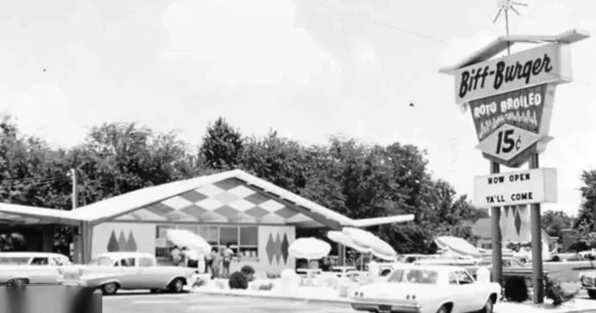 A retro-style diner named 'Biff-Burger' with a checkered awning in an urban area, with cars from the 1950s or early 1960s era.