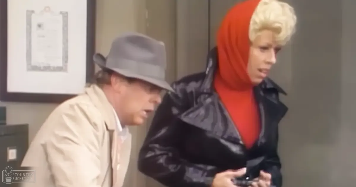 Adult male wearing beige jacket and light-colored fedora hat indoors with woman holding small object or phone; framed document on neutral-colored wall, mid-20th century setting.