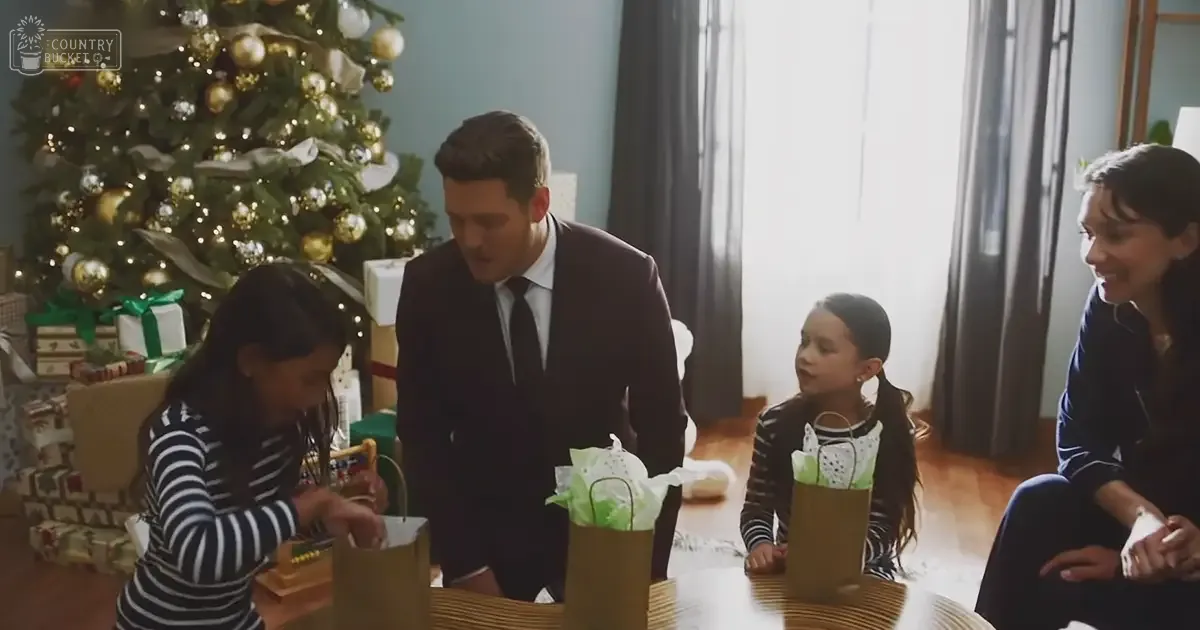 A family scene indoors in a living room decorated for Christmas, with a Christmas tree, presents under it, and natural light coming through windows.
