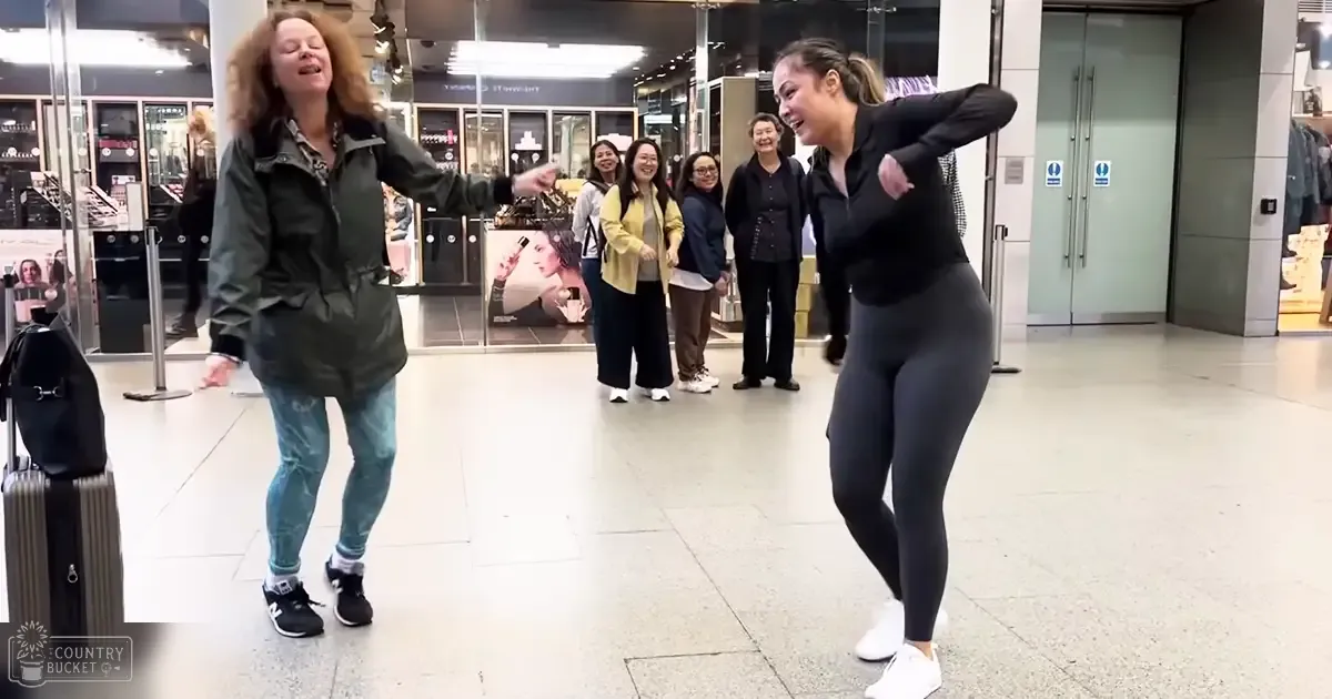 Two women dancing in a shopping mall with glass display cases containing beauty products behind them.