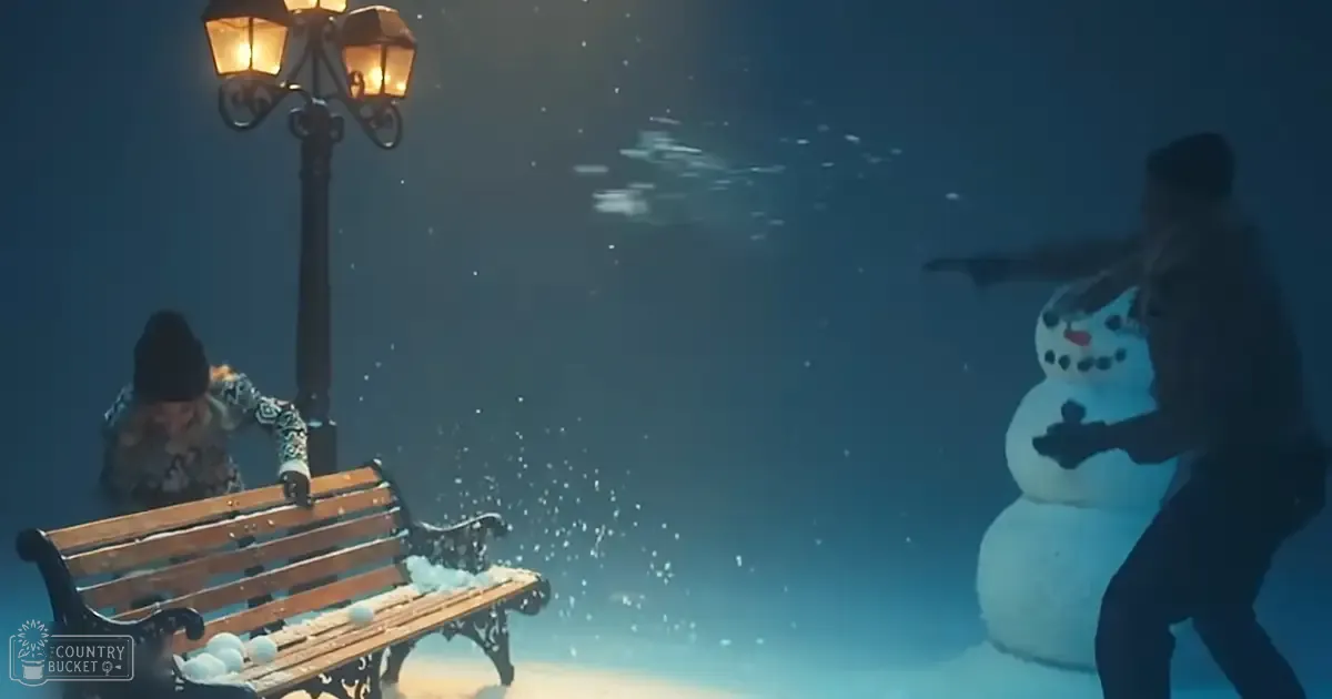 A young adult female in a floral-patterned jacket stands left, an adult male on right in dark attire, under a snow-covered park scene with falling snowflakes and ornate bench.