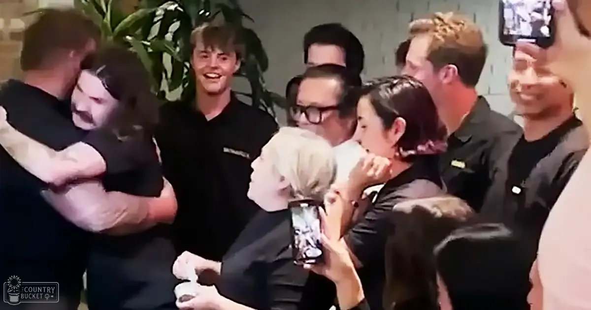 A group celebration indoors with people embracing and holding a smartphone, brick walls in the background, daytime lighting.