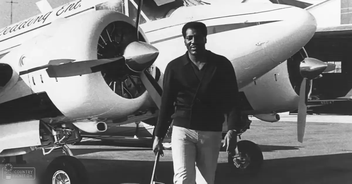 A young adult male stands on an airport tarmac with a large airplane as the backdrop.