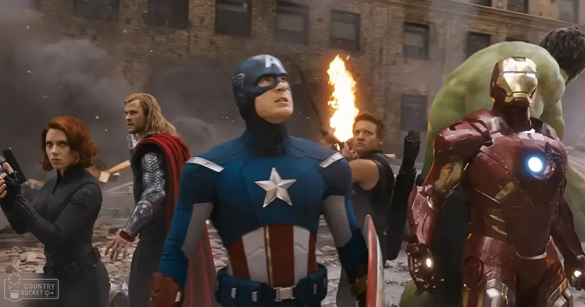 A group of superheroes, including Captain America and Iron Man, stand amidst a backdrop of damaged urban brick buildings with signs of destruction from an explosion or conflict.
