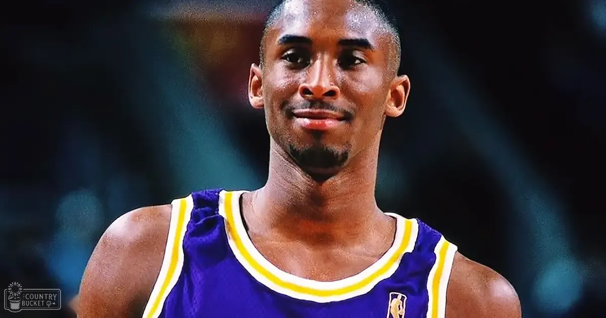 Adult male basketball player wearing a fitted sleeveless purple jersey with white and yellow accents, standing in an indoor arena setting.