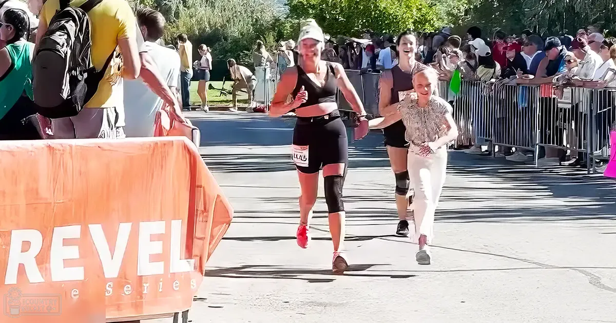 A group of runners participating in Revel Race Series at an outdoor spring or summer event with trees and paved road.